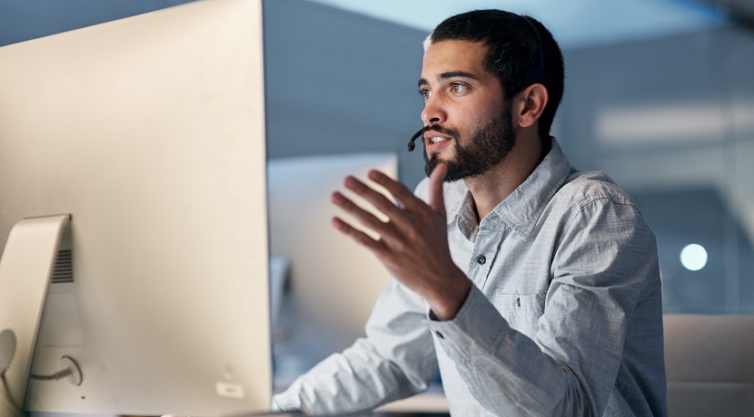 Shot of a young man using a headset and computer late at night in a modern office